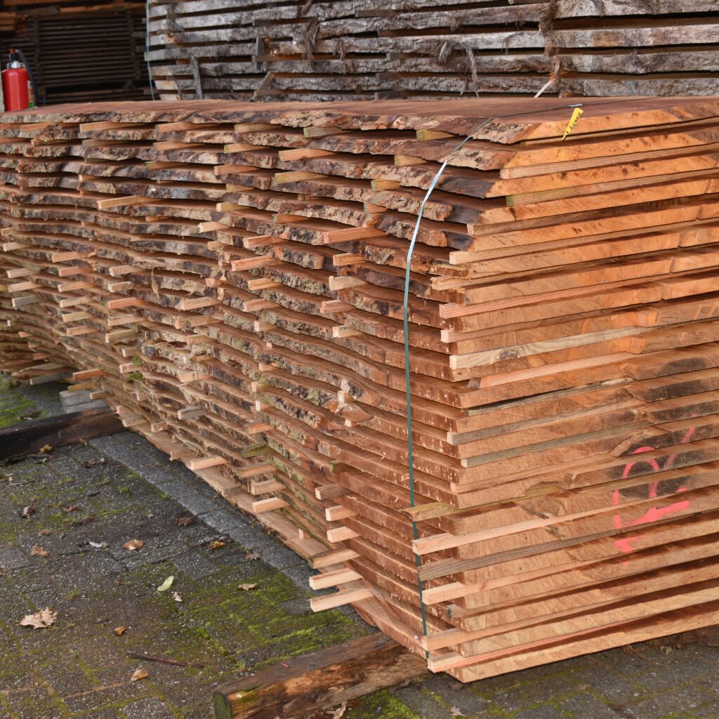 Grote stapel plataanhouten planken met balkjes ertussen op het landgoed van Hard & Zachthout, ideaal voor hoogwaardige houtbewerkingsprojecten.